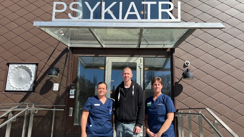 Tre personer i arbetskläder utanför en entré där det står "Psykiatri".