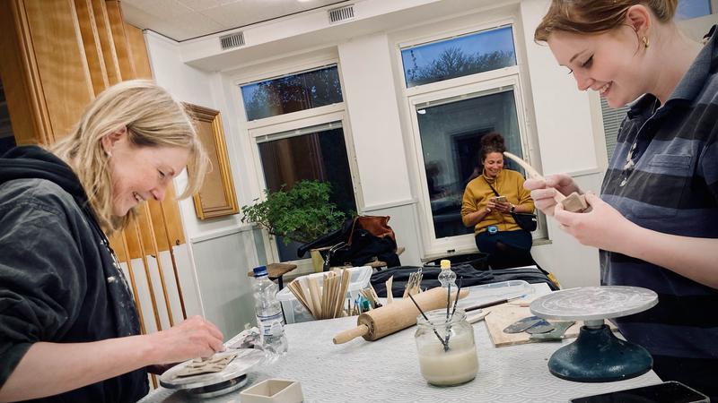 Tre personer jobbar med lera i en stor lokal