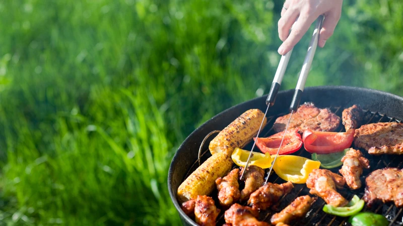 Hand som vänder kött på en grill i naturen, grönt gräs i bakgrunden