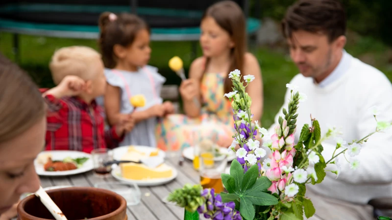blommor i förgrunden vid middagsbord där familj äter