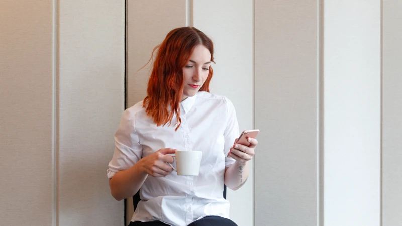 En kvinna sitter på en stol och håller i en kopp kaffe och en telefon.