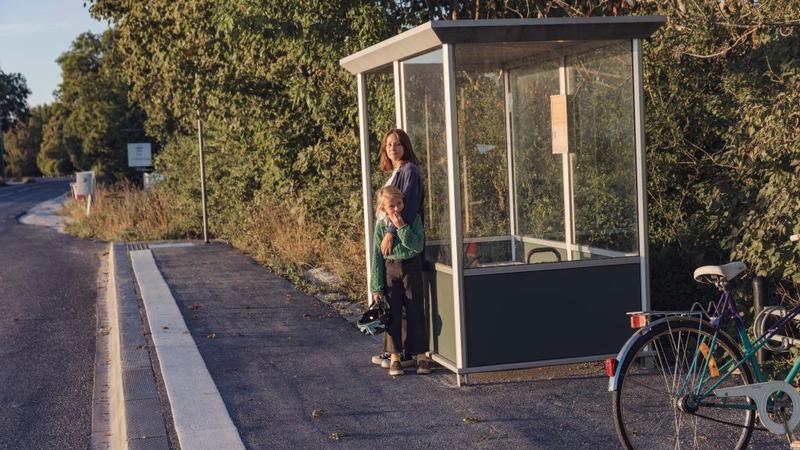 En kvinna som står bredvid en cykel vid en busshållplats.