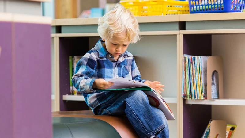 En liten pojke sitter på en boll och läser en bok.