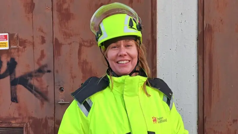 En kvinna i gula arbetskläder och skyddshjälm.