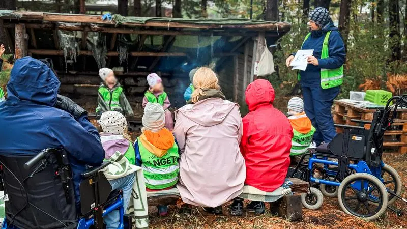 Barn och äldre personer vid ett vindskydd i skogen