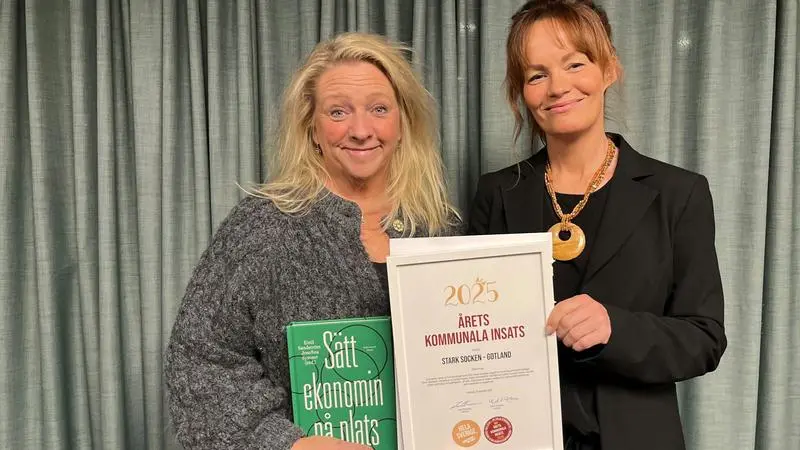 Två kvinnor håller upp en bok och ett diplom.