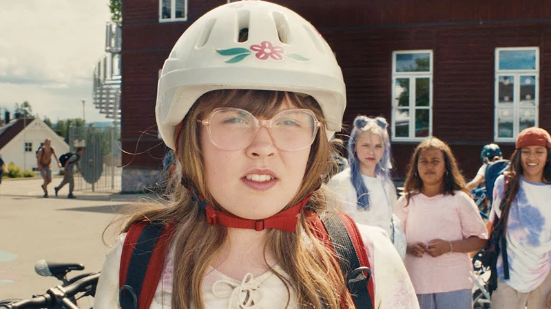 En tjej står med en vit cykelhjälm. I bakgrunden står det 3 unga tjejer till