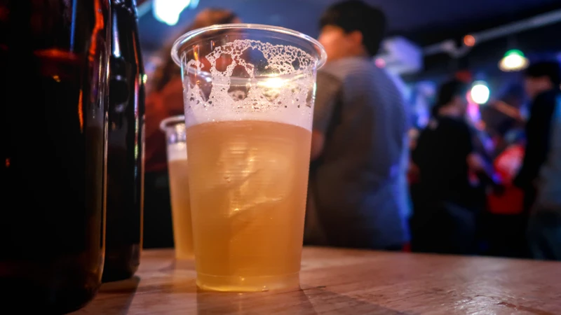 Ett glas öl på ett bord med suddiga människor i bakgrunden.