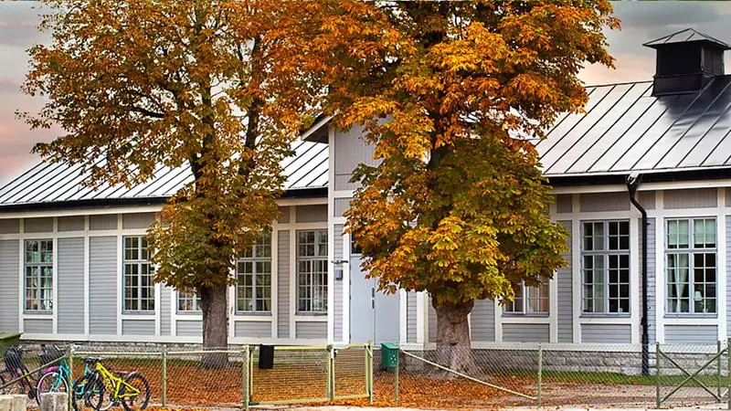 Ett ljusgrått hus med ett träd framför.