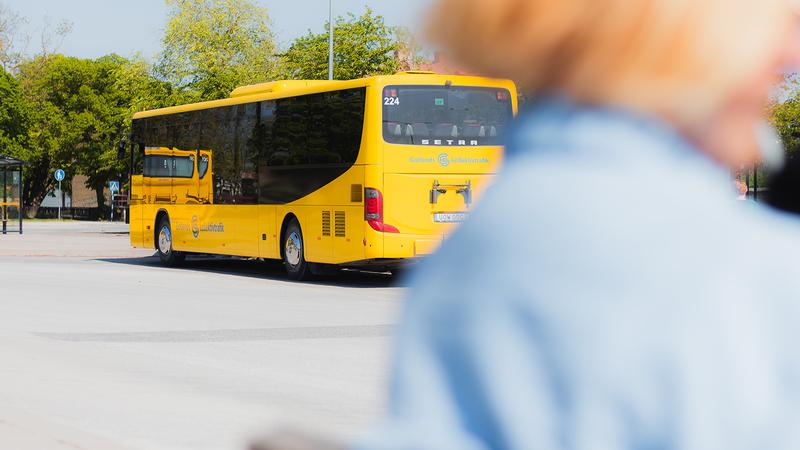 En gul buss kör längs en gata bredvid en kvinna.