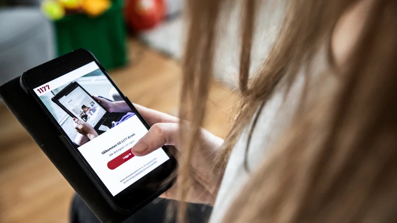 En kvinna håller i en mobiltelefon med en 1177 direkt på skärmen.