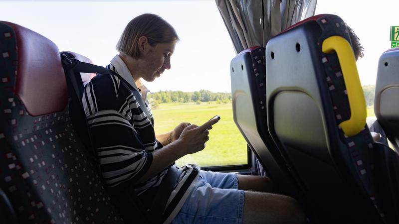 Person sitter på bussen och tittar i en mobiltelefon