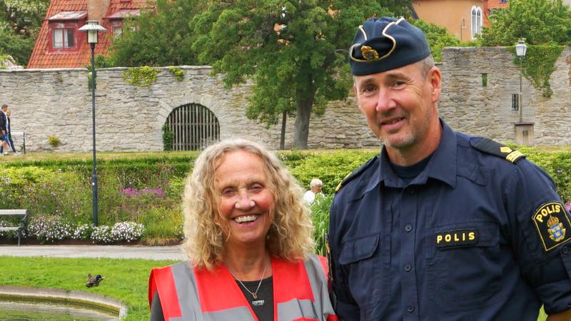 Värd med röd väst och en polis står i Almedalen.