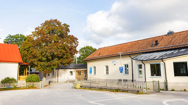 En vit byggnad med rött tak bredvid en parkeringsplats.