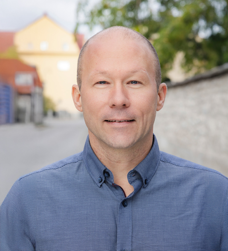 En man i blå skjorta står framför en byggnad.