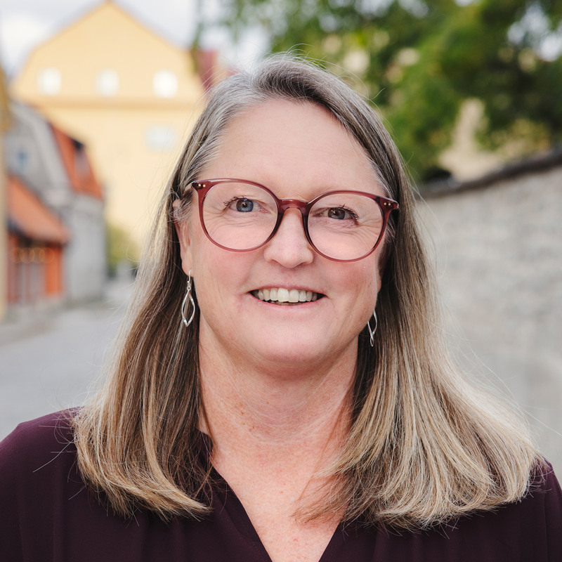 En kvinna med glasögon står framför en tegelvägg.