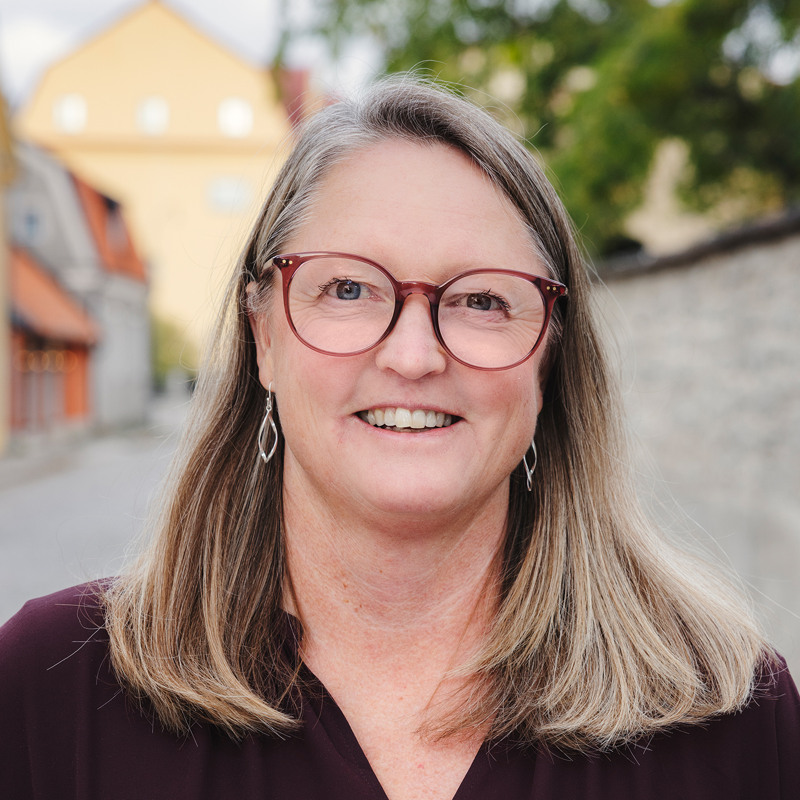 En kvinna med glasögon står framför en tegelvägg.