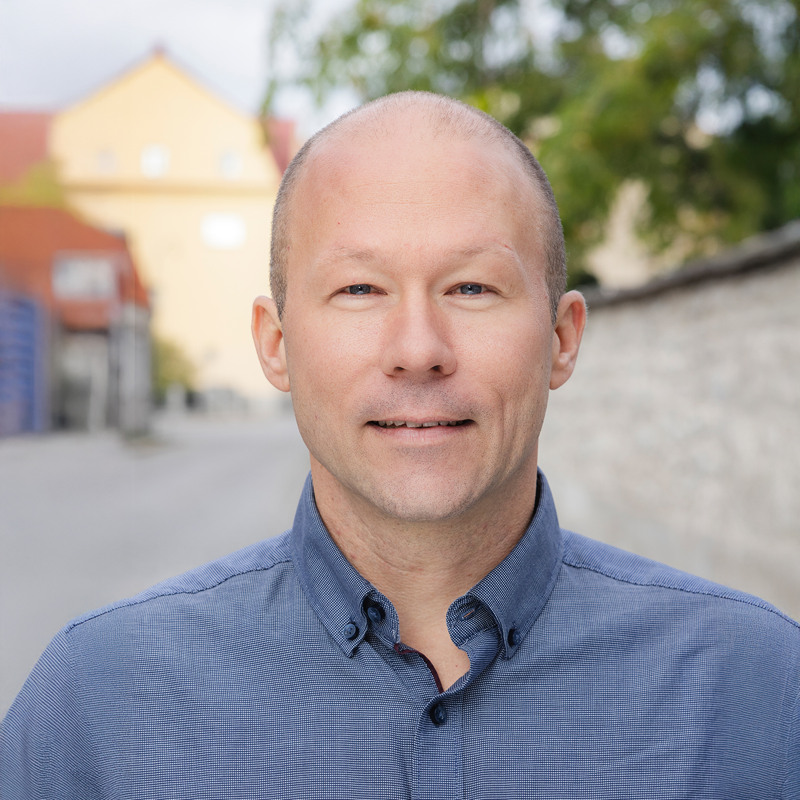 En man i blå skjorta står framför en byggnad.