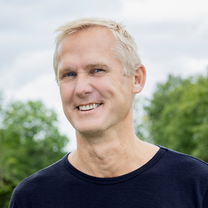 En man i svart skjorta ler mot kameran.