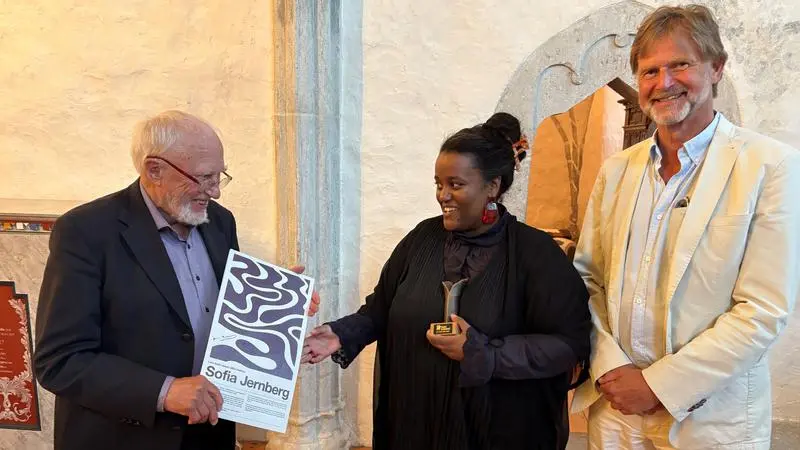 En kvinna tar emot diplom och statyett av en man i en kyrka.