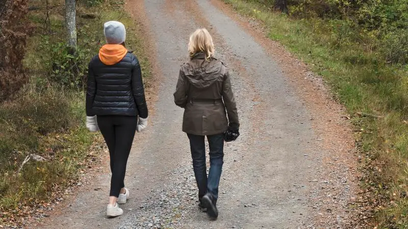 Två personer går på en grusväg i skogen. 