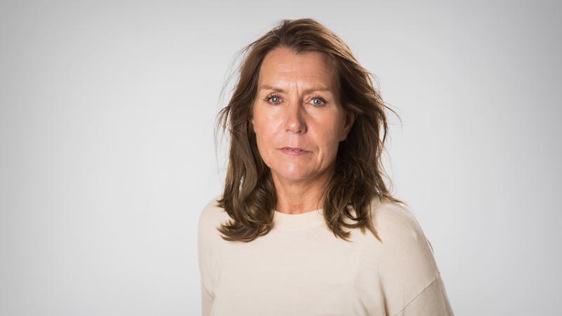 En kvinna i vit tröja står mot en ljusgrå bakgrund.