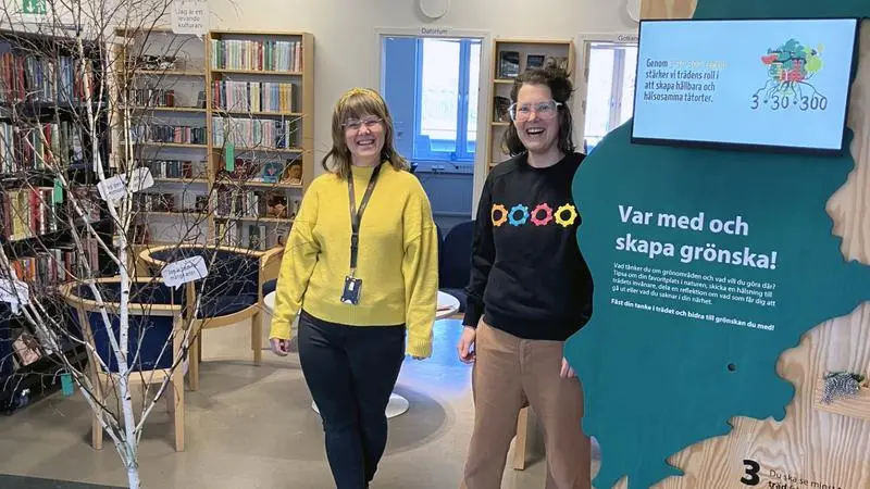 Två glada kvinnor och ett träd på ett bibliotek.