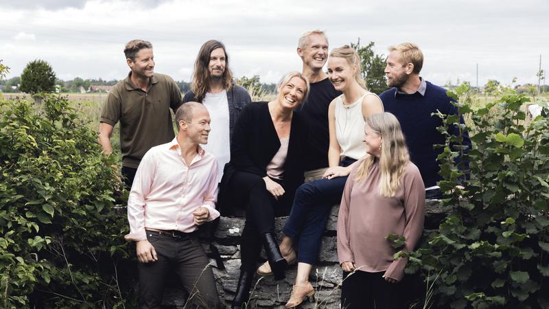 En grupp människor som står, en del sitter bredvid varandra vid en mur
