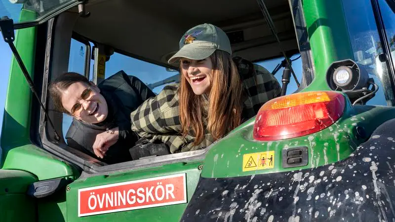 Två tjejer som skrattar och tittar ut genom fönstret på en traktor.