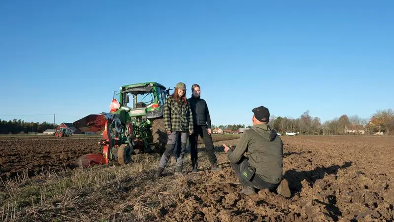 Lärare och elever framför en traktor på en åker.