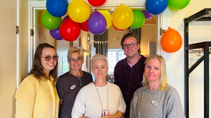 Kollegor står under färgglada ballonger