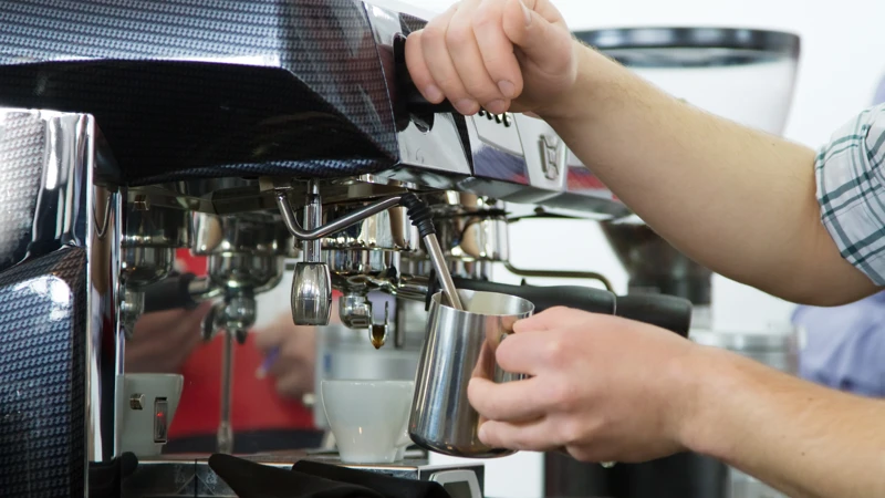 En person skummar mjölk i en espressomaskin.