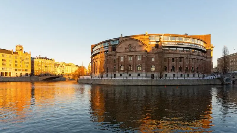 Riksdagshuset i Stockholm intill vattnet i solljus.