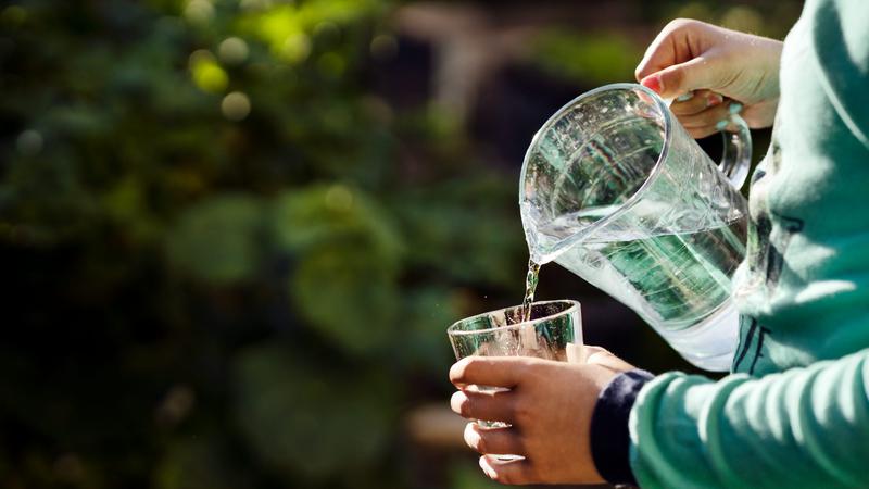 Person häller upp ett glas vatten med en vattenkanna