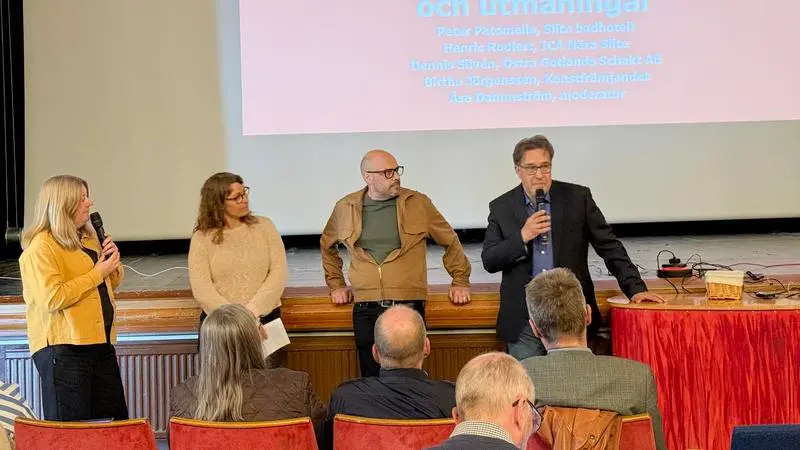 Fyra personer vid en scenkant med en presentation i bakgrunden