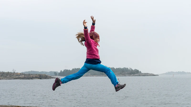 En flicka som hoppar från en klippa ner i vattnet.
