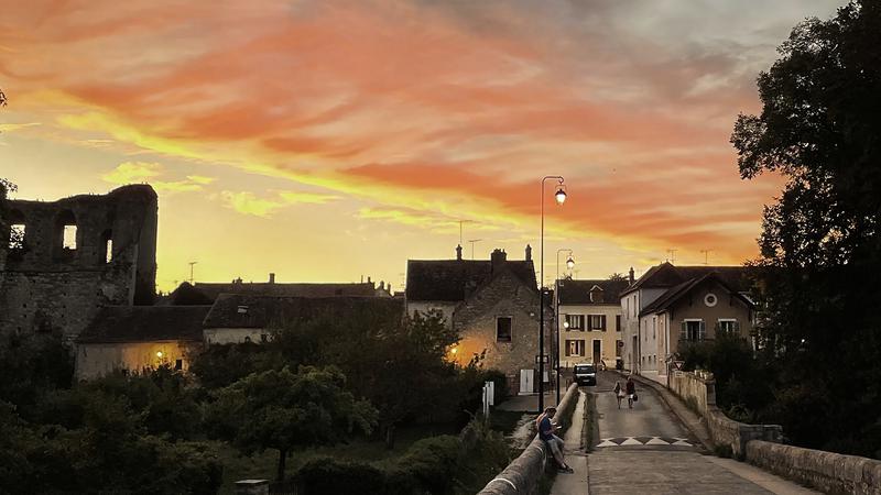 Människor går över en bro i en medeltida stad under en rosa himmel
