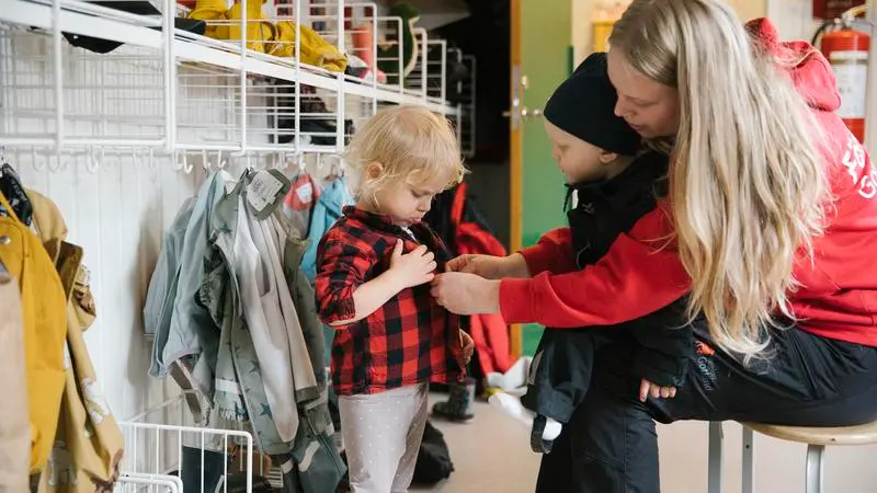 En förskolläarare klär på ett barn i en förskolehall