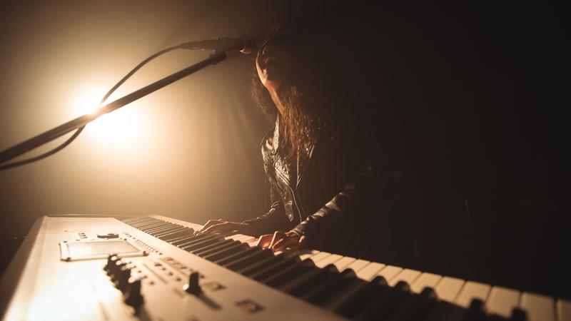 Kvinna sjunger och spelar piano på konsert.