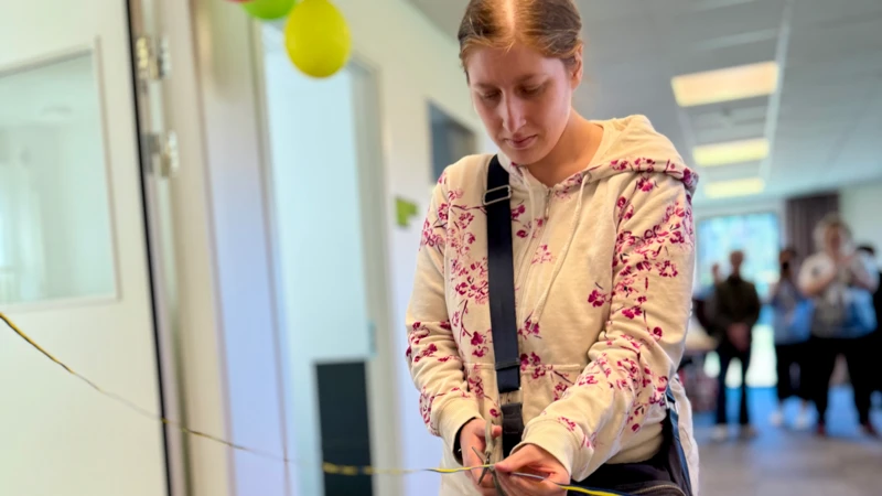 En kvinna i ett rum med ballonger. Hon klipper ett band.