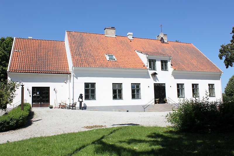 Ett vitt hus med svarta dörrar, blåa fönster och ett rött tak med flera skorstenar.