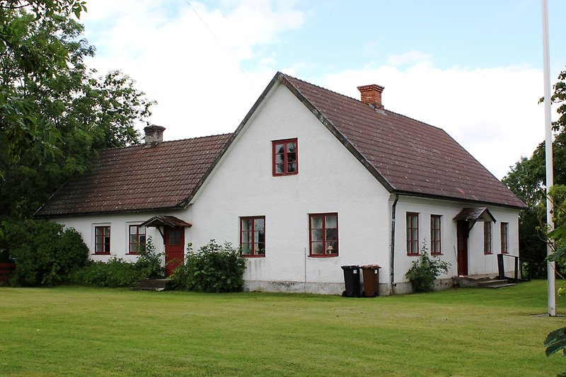 En vit byggnad med röda fönster, röda dörrar och ett rött tak.