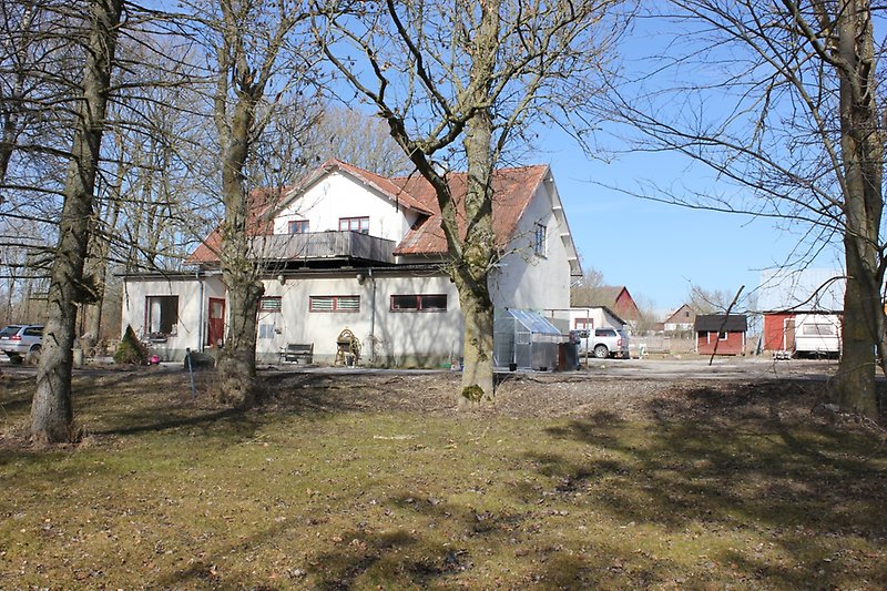 Ett vitt hus med bruna fönster, brun ytterdörr och med ett växthus på gården.