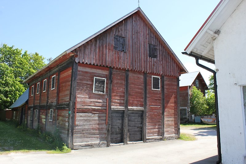 En stor röd ladugård av trä med svarta dörrar och svarta fönster.