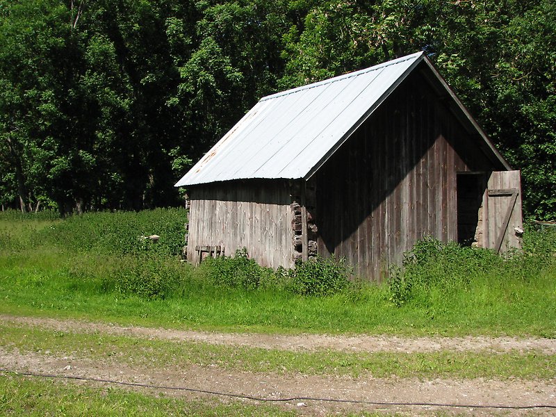 En liten stuga av obehandlat trä som ligger längs en landsväg.