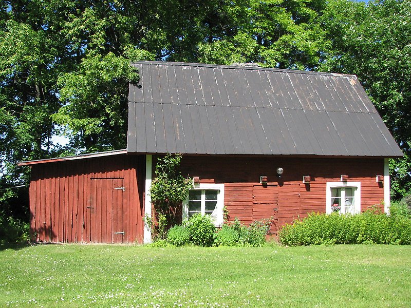 En röd liten stuga med vita fönster och ett svart plåttak.