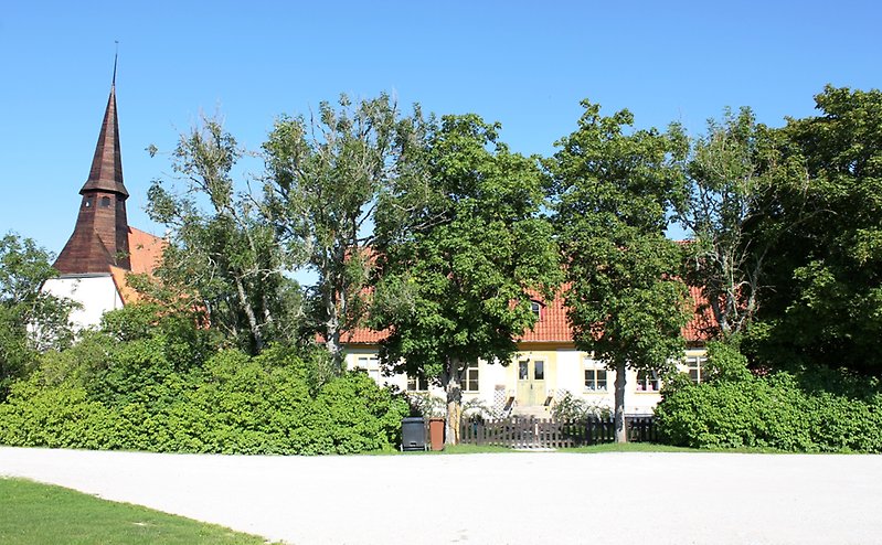 Vänster om ett vitt hus står det en kyrka.