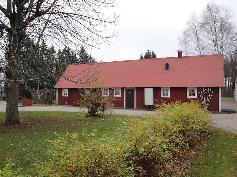 En envånings bygdegård med en svart ytterdörr, röd träfasad, vita fönster och ett rött plåttak med en skorsten.