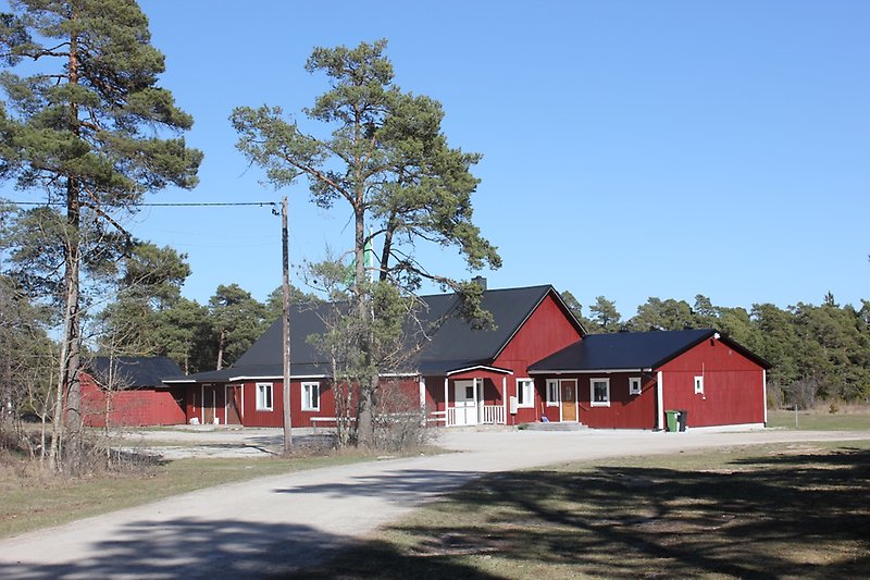 En röd envåningsbyggdegård med vita fönster och ett svart plåttak.