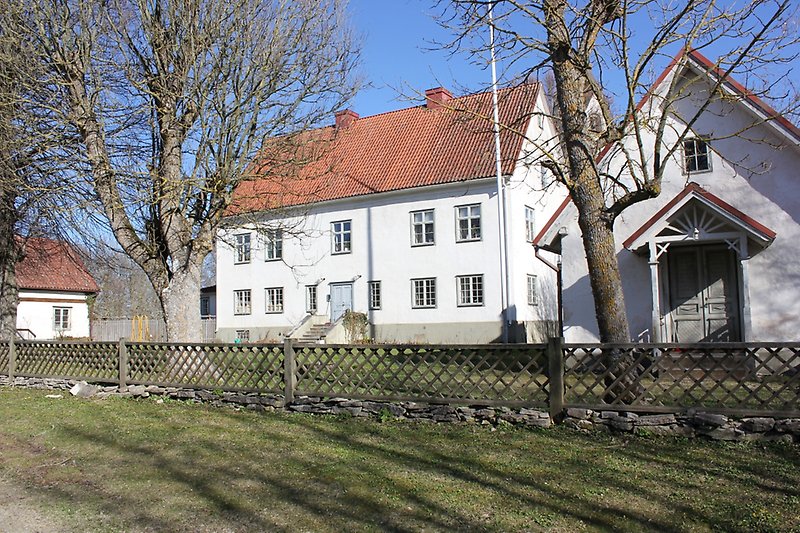 En vit tvåvåningsbyggnad med en ljusblå ytterdörr, vita fönster och ett rött tegeltak med två skorstenar.